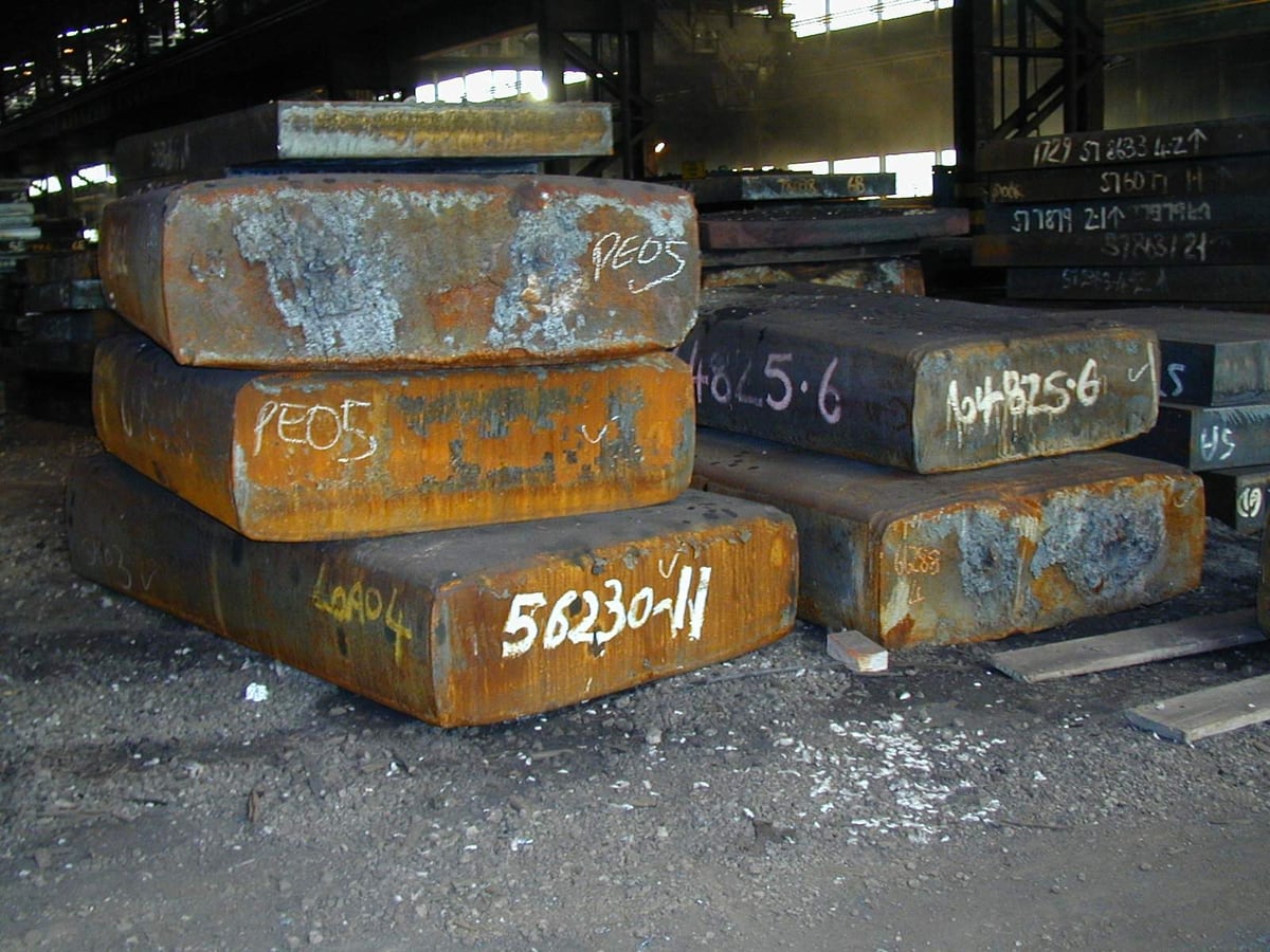 Heavy steel slabs and plate stacked in a yard ready to be cut &mdash; representative imagery, not a specific Late Night Fabrication job